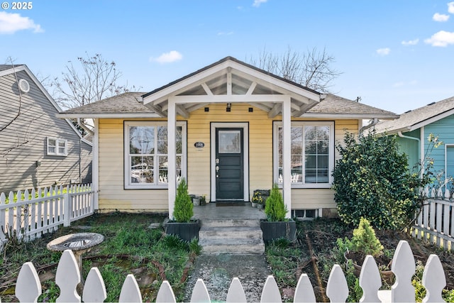 bungalow-style home with a porch, roof with shingles, and fence