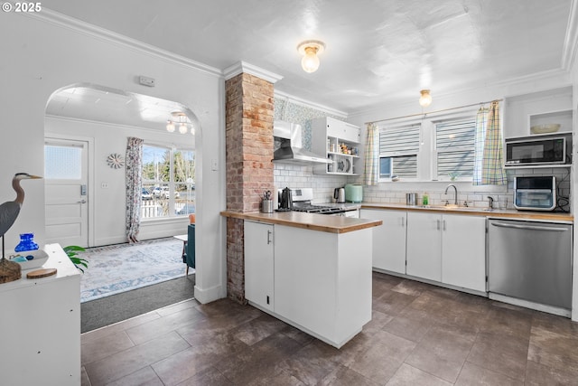 kitchen with arched walkways, appliances with stainless steel finishes, ornamental molding, white cabinetry, and a sink