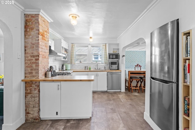 kitchen with arched walkways, a peninsula, stainless steel appliances, crown molding, and backsplash