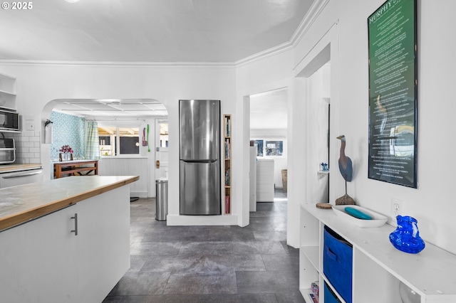 kitchen with appliances with stainless steel finishes, a wealth of natural light, light countertops, and ornamental molding