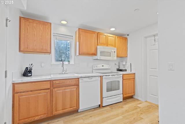 kitchen with white appliances, a sink, light wood finished floors, light countertops, and recessed lighting