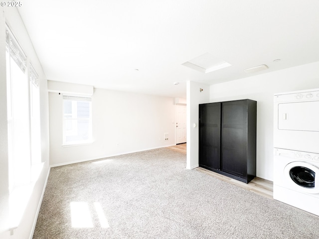spare room featuring stacked washer and clothes dryer, attic access, light carpet, and baseboards