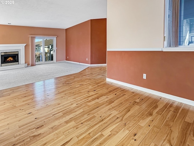 unfurnished living room featuring baseboards, a lit fireplace, and light wood finished floors