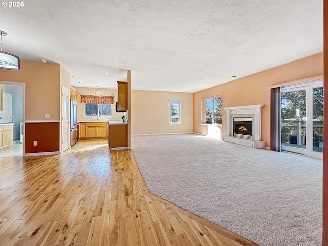 unfurnished living room with a textured ceiling, a healthy amount of sunlight, light wood-style floors, and a lit fireplace