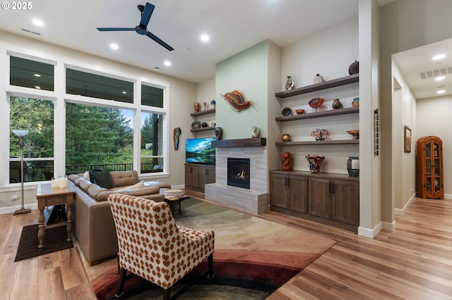 living room featuring ceiling fan, a tiled fireplace, and light wood-type flooring