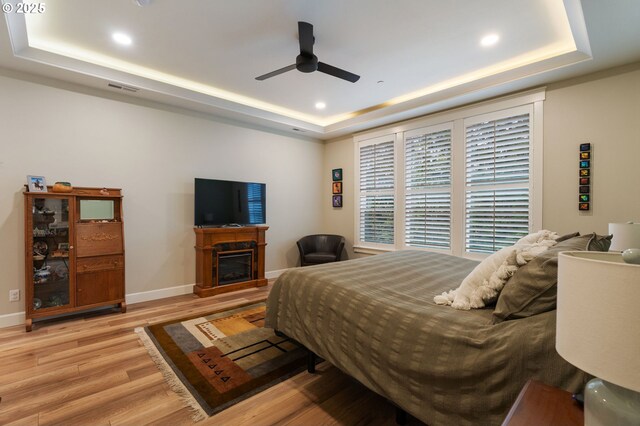 bedroom with ceiling fan, light hardwood / wood-style flooring, ensuite bath, and a tray ceiling