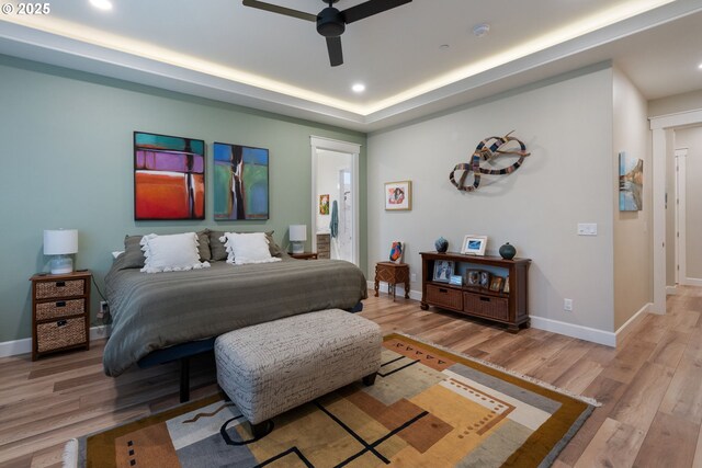 bedroom with ceiling fan, a raised ceiling, and light hardwood / wood-style floors