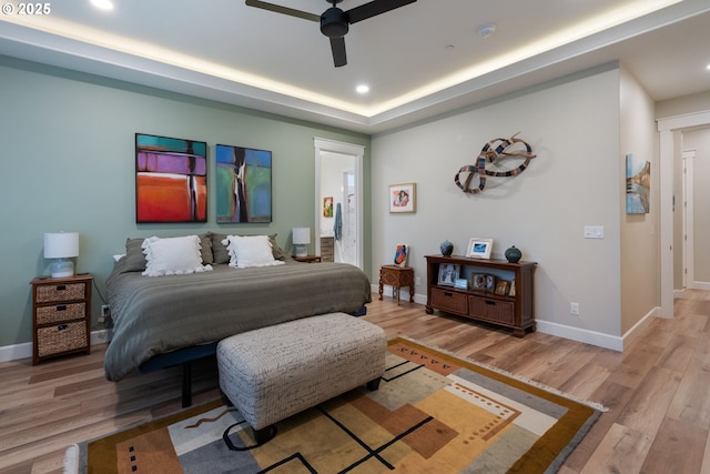 bedroom featuring ceiling fan, a raised ceiling, and light hardwood / wood-style flooring