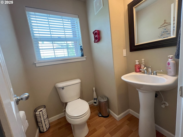half bathroom featuring wood finished floors, toilet, baseboards, and a sink