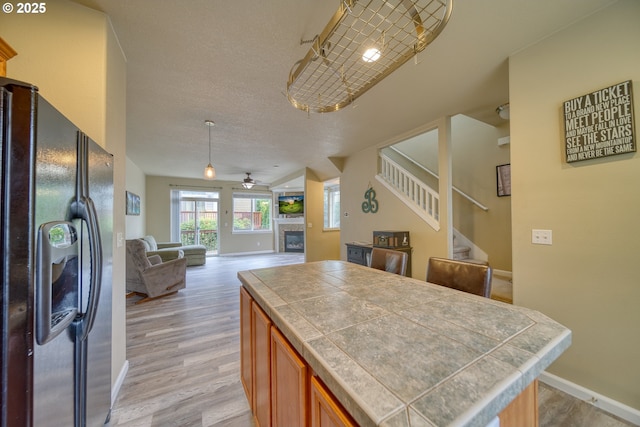 9575 SW Tephra Ter, Beaverton, OR 97007 - kitchen with black fridge, tile counters, a glass covered fireplace, a ceiling fan, and open floor plan