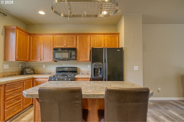 9575 SW Tephra Ter, Beaverton, OR 97007 - kitchen featuring black appliances, a kitchen island, light wood-style floors, tile countertops, and recessed lighting