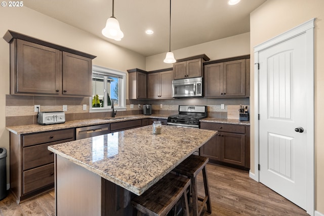 kitchen with dark brown cabinets, stainless steel appliances, wood finished floors, and a sink