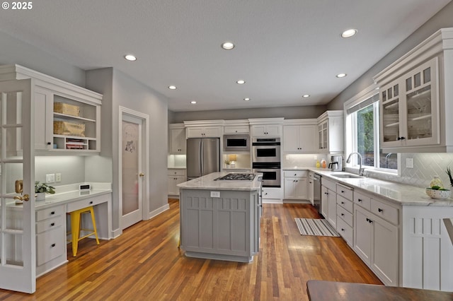 kitchen featuring stainless steel appliances, a sink, light stone countertops, decorative backsplash, and recessed lighting