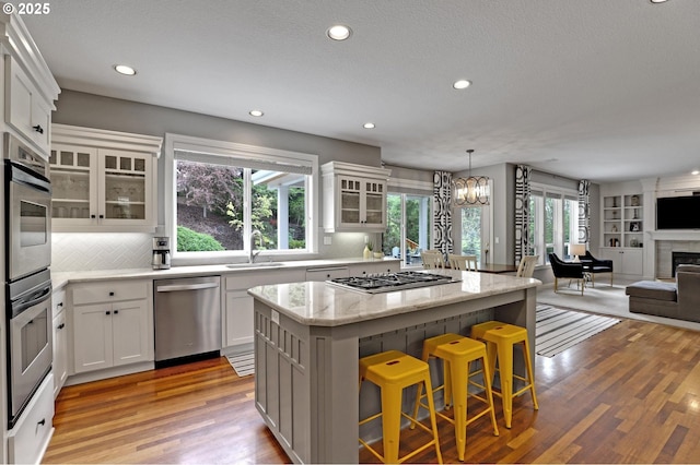 kitchen with stainless steel appliances, open floor plan, a sink, a kitchen island, and light wood-style floors