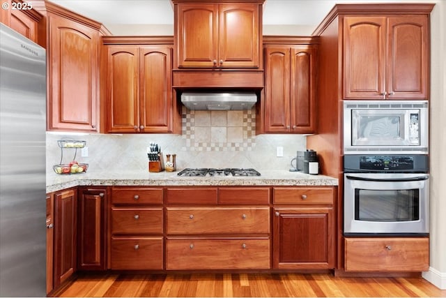 kitchen with tasteful backsplash, wall chimney exhaust hood, stainless steel appliances, and light wood-type flooring