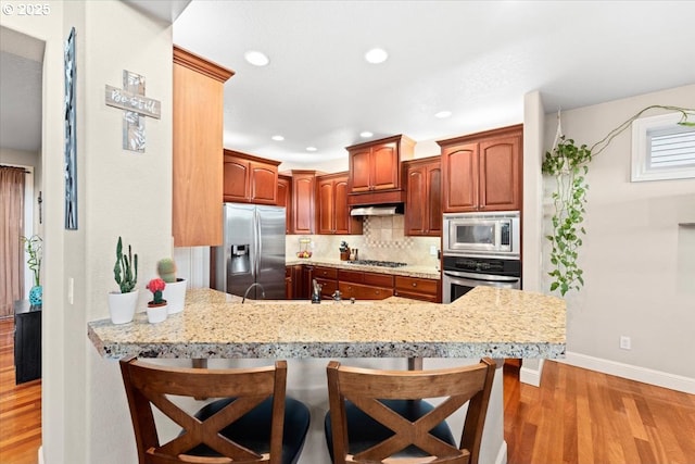 kitchen featuring tasteful backsplash, light hardwood / wood-style floors, a kitchen bar, kitchen peninsula, and stainless steel appliances