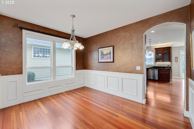 unfurnished dining area with plenty of natural light, a chandelier, and wood-type flooring