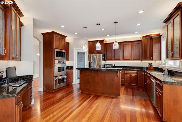 kitchen with stainless steel appliances, sink, decorative light fixtures, hardwood / wood-style floors, and a center island