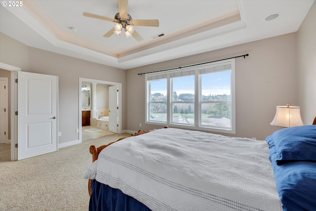 carpeted bedroom with a tray ceiling, ensuite bath, and ceiling fan