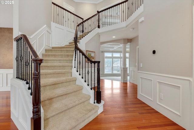 staircase with ornate columns, hardwood / wood-style floors, and a towering ceiling