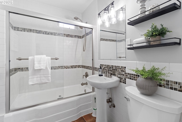 bathroom featuring toilet, a sink, bath / shower combo with glass door, and tile walls