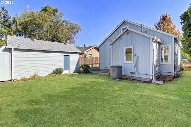 back of property with central air condition unit, a shingled roof, fence, and a lawn