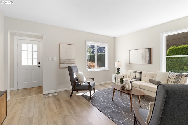 living room with light wood-style floors, visible vents, and baseboards