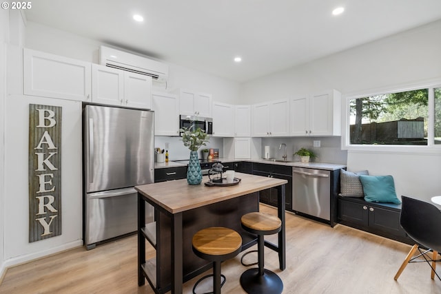 27650 SW Canyon Creek Rd, Wilsonville, OR 97070 - kitchen featuring stainless steel appliances, a wall unit AC, a sink, light wood-type flooring, and white cabinetry