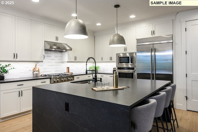 kitchen featuring sink, backsplash, hanging light fixtures, built in appliances, and light wood-type flooring