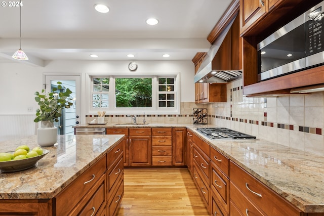 kitchen with light stone countertops, pendant lighting, appliances with stainless steel finishes, sink, and light hardwood / wood-style flooring