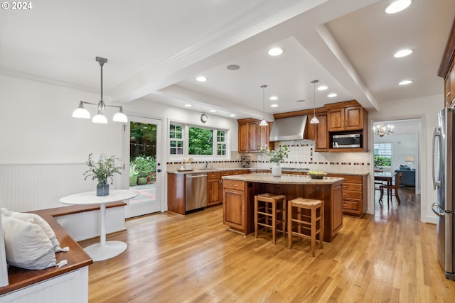 kitchen featuring appliances with stainless steel finishes, wall chimney exhaust hood, decorative light fixtures, and a center island