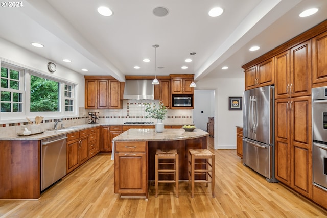 kitchen with a center island, decorative light fixtures, wall chimney range hood, stainless steel appliances, and light stone counters