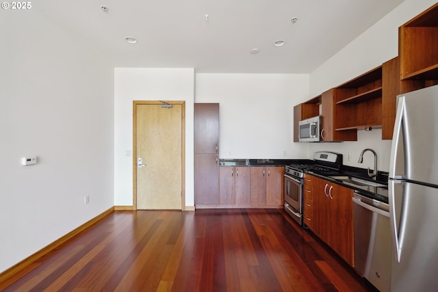 kitchen with appliances with stainless steel finishes, open shelves, a sink, dark countertops, and dark wood-type flooring
