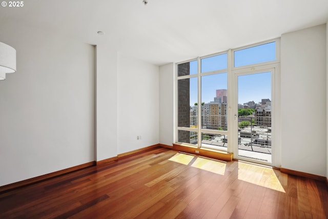 empty room featuring a city view, hardwood / wood-style flooring, baseboards, a wall of windows, and fire sprinkler in ceiling