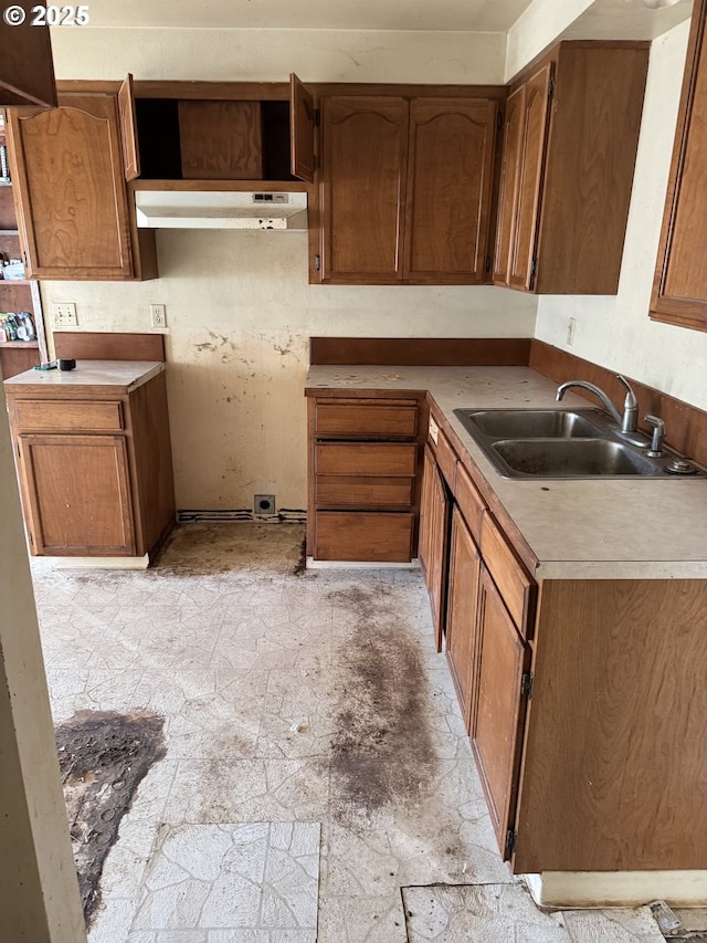 kitchen with stone finish floor, brown cabinets, under cabinet range hood, and a sink