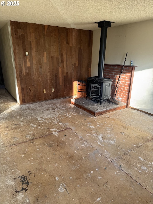 unfurnished living room featuring wooden walls, a textured ceiling, and a wood stove