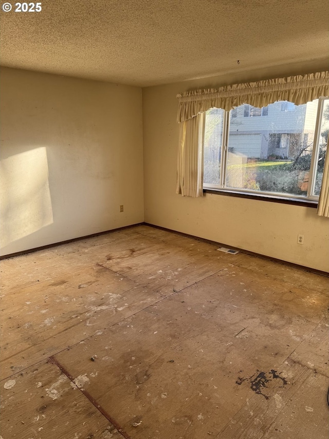 spare room featuring baseboards, a healthy amount of sunlight, visible vents, and a textured ceiling