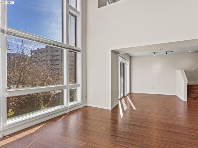 empty room with dark wood-type flooring, a towering ceiling, and a wealth of natural light