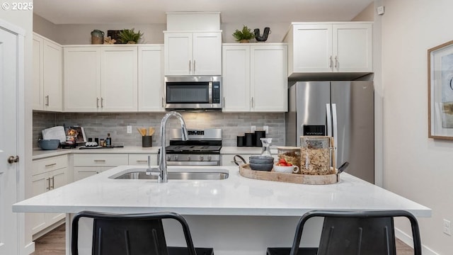 kitchen with white cabinets, a sink, a kitchen island with sink, stainless steel appliances, and tasteful backsplash