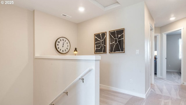 hallway featuring baseboards, visible vents, light carpet, and an upstairs landing