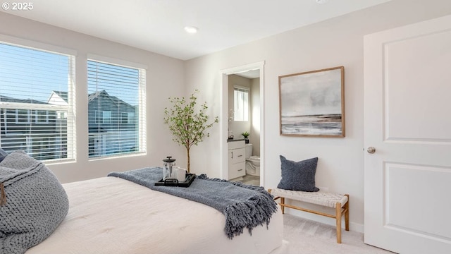 bedroom with baseboards, ensuite bathroom, and light carpet