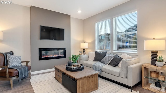 living room with baseboards, a glass covered fireplace, and light wood-style floors