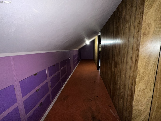 hall featuring carpet floors, vaulted ceiling, and a textured ceiling