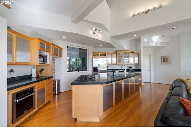 kitchen featuring sink, light wood-type flooring, an island with sink, stainless steel appliances, and beam ceiling