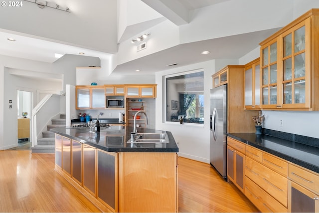 kitchen with sink, dark stone countertops, light wood-type flooring, appliances with stainless steel finishes, and an island with sink