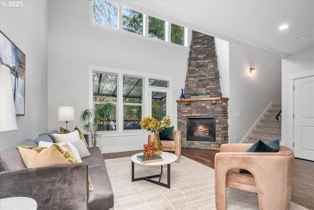 living area with wood finished floors, recessed lighting, stairway, a fireplace, and a towering ceiling