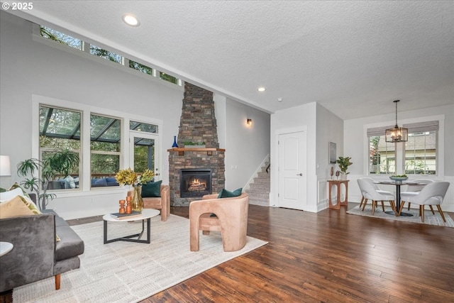 living area with a notable chandelier, hardwood / wood-style flooring, a textured ceiling, stairway, and a stone fireplace