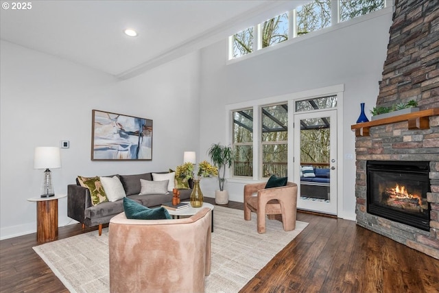 living area featuring a stone fireplace, a high ceiling, baseboards, and wood-type flooring