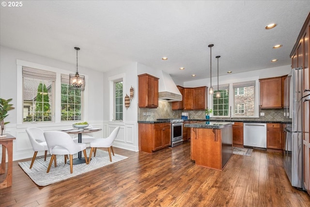 kitchen with a wealth of natural light, custom range hood, appliances with stainless steel finishes, and a kitchen island