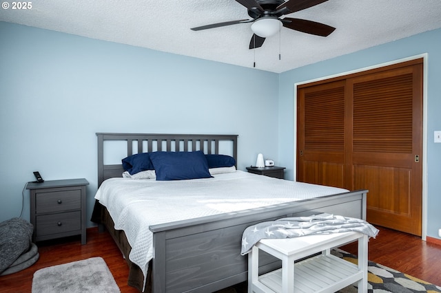 bedroom featuring dark wood-type flooring, ceiling fan, a closet, and a textured ceiling